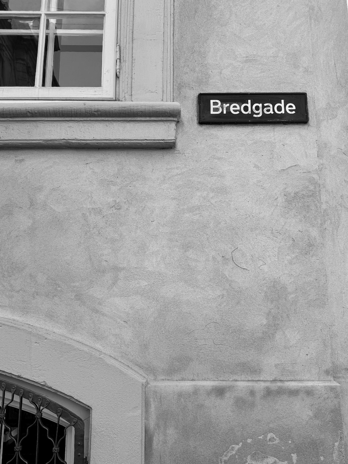 Gatuskylt Bredgade på putsad fasad — svartvitt